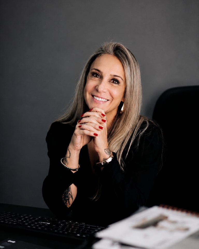 Dra. Marcela Noronha sorrindo, com as mãos apoiadas, em seu escritório